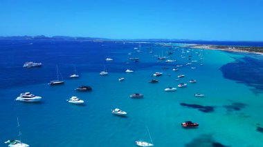 Formentera yüksek sosyetesinden Balear Adası 'nın berrak turkuaz sularına demirlemiş pek çok zevk teknesinin havadan görüntüsü. durağan tripod havada süzülen panorama drone