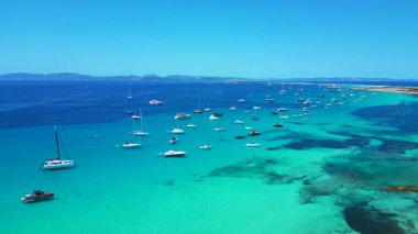 Formentera yüksek sosyetesinden Balear Adası 'nın berrak turkuaz sularına demirlemiş pek çok zevk teknesinin havadan görüntüsü. durağan tripod havada süzülen panorama drone