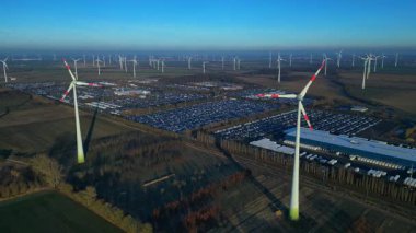 Geniş bir araba dağıtım merkezi ve araç parkına yenilenebilir enerji sağlayan büyük bir rüzgar çiftliği. panorama genel görünüm dronu