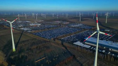 Geniş bir araba dağıtım merkezi ve araç parkına yenilenebilir enerji sağlayan büyük bir rüzgar çiftliği. Ters panorama görünümü dronu uçur