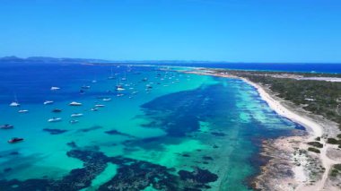 Posidonia Oceanica 'nın beyaz kumlu sahili Formentera' nın nefes kesici turkuaz sularında demirleyen tekneler. İHA panorama genel görüntüsü alçalıyor