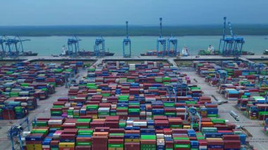 Sayısız nakliye konteynırı, kanat vinci ve kargo gemisi olan büyük bir konteynır limanının havadan görüntüsü. Yukarıdan aşağıya doğru uçur