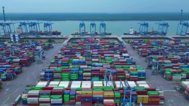 Sayısız nakliye konteynırı, kanat vinci ve kargo gemisi olan büyük bir konteynır limanının havadan görüntüsü. Uçarken üstten uçmak İHA 'yı ileri itmek