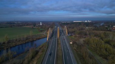 Sakin bir nehir üzerinde otoban taşıyan modern kemer köprüsü bulutlu bir günde kırsal araziyi birbirine bağlıyor. statik panorama havada süzülen drone