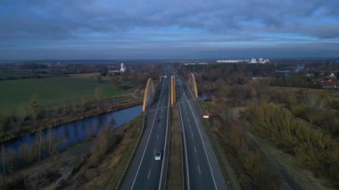 Sakin bir nehir üzerinde otoban taşıyan modern kemer köprüsü bulutlu bir günde kırsal araziyi birbirine bağlıyor. panorama genel görünüm dronu
