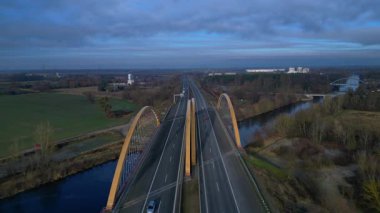 Sakin bir nehir üzerinde otoban taşıyan modern kemer köprüsü bulutlu bir günde kırsal araziyi birbirine bağlıyor. statik panorama havada süzülen drone