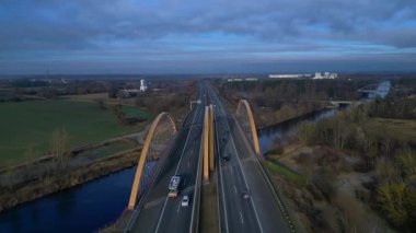 Sakin bir nehir üzerinde otoban taşıyan modern kemer köprüsü bulutlu bir günde kırsal araziyi birbirine bağlıyor. Uçuş üstlerinden ters uç, panorama göz gezdirme aracı.
