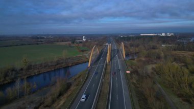 Sakin bir nehir üzerinde otoban taşıyan modern kemer köprüsü bulutlu bir günde kırsal araziyi birbirine bağlıyor. statik panorama havada süzülen drone