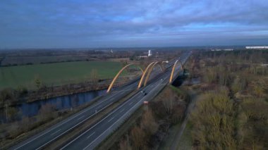 Sakin bir nehir üzerinde otoban taşıyan modern kemer köprüsü bulutlu bir günde kırsal araziyi birbirine bağlıyor. Geniş yörünge panorama görünümü insansız hava aracı