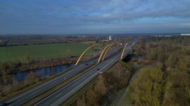Sakin bir nehir üzerinde otoban taşıyan modern kemer köprüsü bulutlu bir günde kırsal araziyi birbirine bağlıyor. statik panorama havada süzülen drone