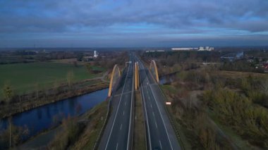 Sakin bir nehir üzerinde otoban taşıyan modern kemer köprüsü bulutlu bir günde kırsal araziyi birbirine bağlıyor. Sinek ileri itme panorama genel görünüm drone