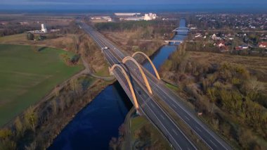 Modern Alman otoyol köprüsünün hız rampası nehir üzerinde araç trafiğini taşıyor ve peyzajları birbirine bağlıyor. Geniş yörünge panorama görünümü insansız hava aracı