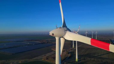 Rüzgâr türbinlerinin son sürat giden hız rampası dönüyor, büyük bir rüzgar çiftliği, sanayi tesisleri ve aşağıdaki otoparkta temiz yenilenebilir enerji üretiyor. statik panorama havada süzülen drone