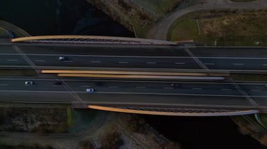 Modern Alman otoyol köprüsünün hız rampası nehir üzerinde araç trafiğini taşıyor ve peyzajları birbirine bağlıyor. Aşağıya bakan İHA kamerası