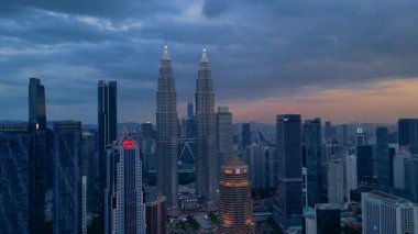 Kuala Lumpur şehrinin silueti, kasvetli bir günbatımı sırasında diğer modern gökdelenlerle çevrili ikonik Petronas İkiz Kuleleri ile çevrilidir. rotasyon pan 'dan sağ drona