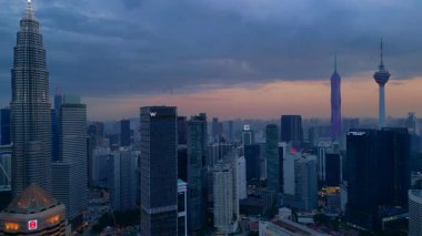 Kuala Lumpur şehrinin silueti, kasvetli bir günbatımı sırasında diğer modern gökdelenlerle çevrili ikonik Petronas İkiz Kuleleri ile çevrilidir. Yukarıdan drone atışı