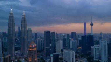 Kuala Lumpur şehrinin silueti, kasvetli bir günbatımı sırasında diğer modern gökdelenlerle çevrili ikonik Petronas İkiz Kuleleri ile çevrilidir. panorama genel görünüm dronu