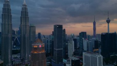Kuala Lumpur şehrinin silueti, kasvetli bir günbatımı sırasında diğer modern gökdelenlerle çevrili ikonik Petronas İkiz Kuleleri ile çevrilidir. Panorama genel bakış insansız hava aracı yükseliyor