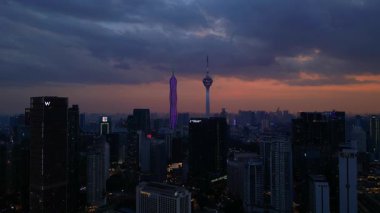 Kuala Lumpur şehri, kentsel gelişimi temsil eden aydınlık Merdeka 118 gökdeleni ve KL Kulesi 'nin yer aldığı güzel bir günbatımında ufuk çizgisine sahiptir. İHA alçalıyor