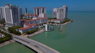 Modern yüksek binalar, konut evleri, arabalı köprü ve okyanus kıyısında marinası olan tropik şehir manzarası. statik panorama havada süzülen drone