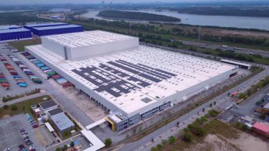 Çatıda çok sayıda yükleme limanı, nakliye konteynırları ve güneş panellerinin yer aldığı büyük lojistik binalar, sürdürülebilirliği vurguluyor. Geniş yörünge panorama görünümü insansız hava aracı