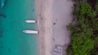 Gili Trawangan kıyıları turkuaz su ve kumlu sahilde demirli tekneleri gösteriyor. Aşağıya bakan İHA kameraları yükseliyor
