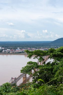 Pakse köprüsü mekong nehrine yayılıyor, yemyeşil ormanı ve şehir gelişimini bulutlu bir gökyüzü altında birbirine bağlıyor