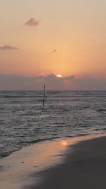 Altın güneş Sri Lanka 'da geleneksel bir balıkçı direğiyle sakin bir okyanusun üzerinde batıyor.