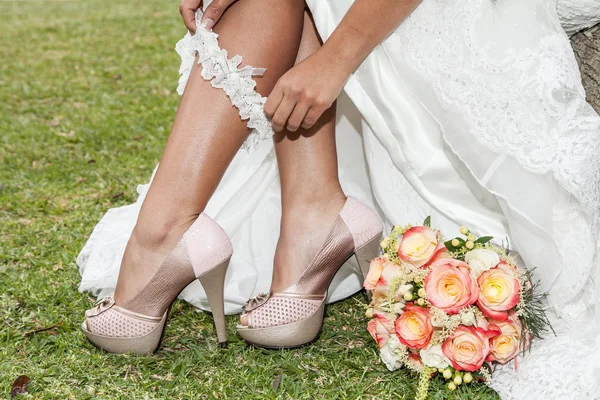 Close-up de mulher colocando liga com sapatos e buquê de flores — Fotografia de Stock
