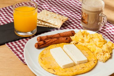 Tasty traditional breakfast in Colombia; Arepa of yellow corn with cheese, scrambled eggs and sausages. clipart
