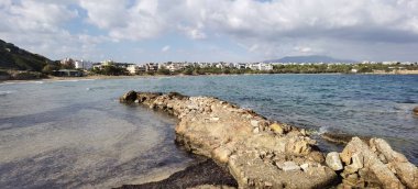 Önde yürünebilir bir yarımadanın olduğu güzel bir panoramik manzara denize doğru uzanır ve arka planda Marikes Sahili görünür. Sakin yaz suları, yukardaki yumuşak bulutlar ve Yunanistan 'ın Rafina, Attica kentindeki kıyı şeridi manzarası. İdeal 