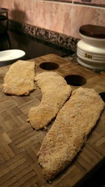 Ev mutfağındaki kesme tahtasının üzerinde duran un ve çırpılmış yumurtalı taze kızarmış tavuk filetoları..