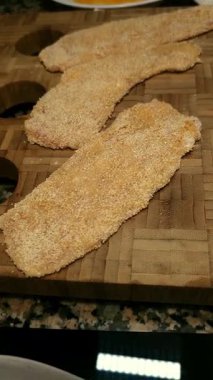 Ev mutfağındaki kesme tahtasının üzerinde duran un ve çırpılmış yumurtalı taze kızarmış tavuk filetoları..