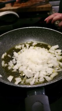 Bir kadın elinin sıcak tavada doğranmış soğana zeytinyağlı bir tutam tuz eklemesi. Sağlıklı aşçılık kavramı.
