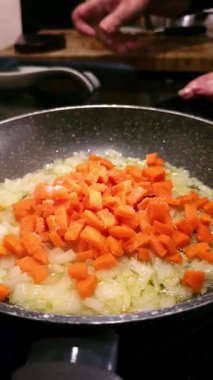 Bir kadın elinin sıcak tavada doğranmış soğan ve havuç ve zeytinyağına bir tutam tuz eklemesi. Sağlıklı aşçılık kavramı.