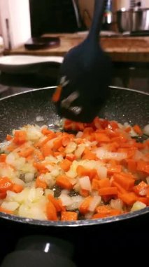 Bir kadının elleri zeytinyağlı tavada doğranmış havuç ve soğan karıştırıyor. Sağlıklı aşçılık kavramı.