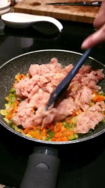 Bir kadının elleri tavuğu, doğranmış havucu ve zeytinyağlı bir tavada soğanı karıştırıyor. Sağlıklı aşçılık kavramı.