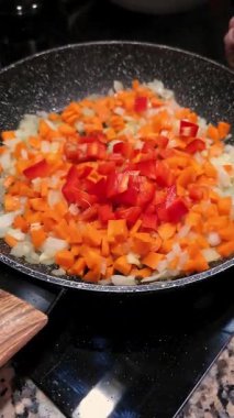 Kızarmış soğan ve havuç kızartma kabına kırmızı biber ekleniyor. Evde yemek pişirmek..