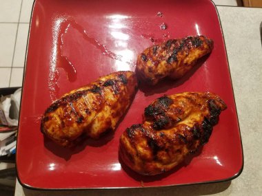 Kırmızı tabakta ızgara sosla kaplanmış üç ızgara tavuk göğsü. Yüksek kalite fotoğraf