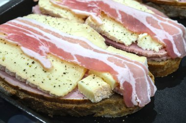 Ekmek, peynir, jambon ve biberli çiğ pastırma dilimli açık sandviçler kırsal mutfak ortamında pişirilmeye hazır..