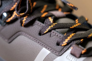 Turuncu aksanlı, tekstil ve deri karışımlı spor ayakkabıları, zanaatkarlığı ve kentsel tarzı gösteriyor. Dikişlere yakın çekim.