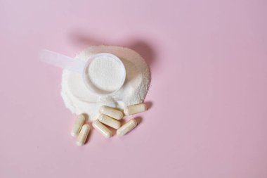 Pembe arka planda destek kapsüllü kolajen ya da protein tozu kepçesi, refah, güzellik, beslenme ve fitness markalaşması için minimalist stüdyo konsepti. Üst görünüm.