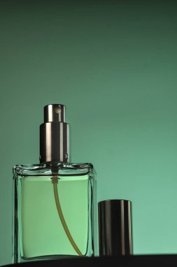 Açık yeşil sıvı, metalik püskürtme başlığı ve yeşil eğimli kapağı olan temiz cam parfüm şişesine yakın plan..