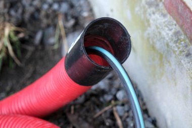 Açık hava tesisatı kurulumu sırasında tuğla ev temelinin yanında kırmızı kablo bobini ve siyah kablo bobini. Kapat..