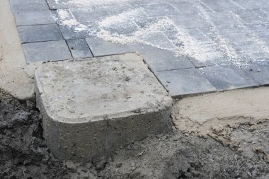 Yeni yerleştirilmiş veranda kaldırımları birleşmek için kumla kaplı, beton ocak ve gelecekteki pergola kurulumu için köşe blokları ile sınırlandırılmış. Bir köşe bloğunu kapat.