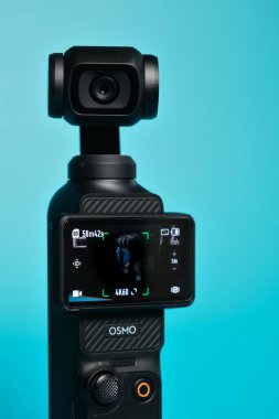 Wallers, Fransa - 02 20 2026: DJI Osmo Pocket 3 kompakt kamera turkuaz arka planda motorlu el kamerası, vloglama ve sinematik video oluşturma için ideal. Kamera selfie modunda..