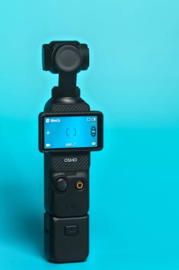 Wallers, Fransa - 02 20 2026: DJI Osmo Pocket 3 kompakt kamera turkuaz arka planda motorlu el kamerası, vloglama ve sinematik video oluşturma için ideal. Genel bakış. Camra açıldı.