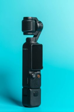 Wallers, Fransa - 02 20 2026: DJI Osmo Pocket 3 kompakt kamera turkuaz arka planda motorlu el kamerası, vloglama ve sinematik video oluşturma için ideal. Genel portre görünümü.