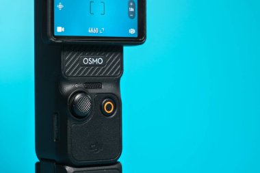 Wallers, Fransa - 02 20 2026: DJI Osmo Pocket 3 kompakt kamera turkuaz arka planda motorlu el kamerası, vloglama ve sinematik video oluşturma için ideal. Oyun kumandasına odaklan.