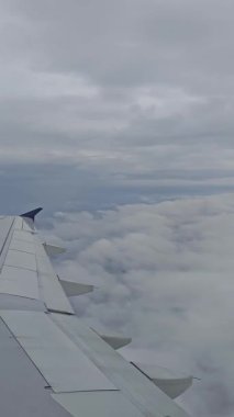 Uçak kanadı yoğun beyaz bulutlar üzerinde belirgin bir şekilde uzanır. Ticari bir uçuşla sessiz ve gri bir gökyüzü üzerinde seyahat etmeyi önerir..